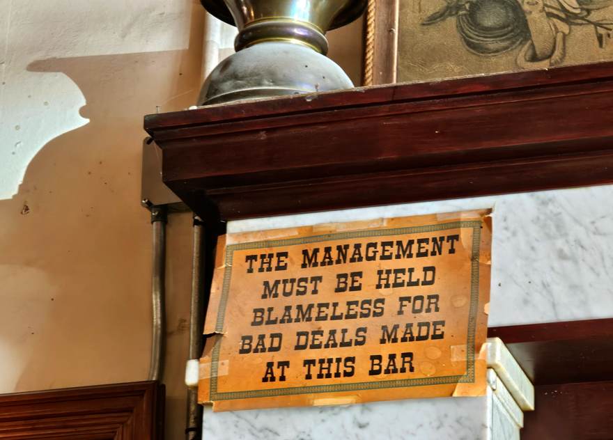 Bar sign reading The Management Must Be Held Blameless For Bad Deals Made At This Bar