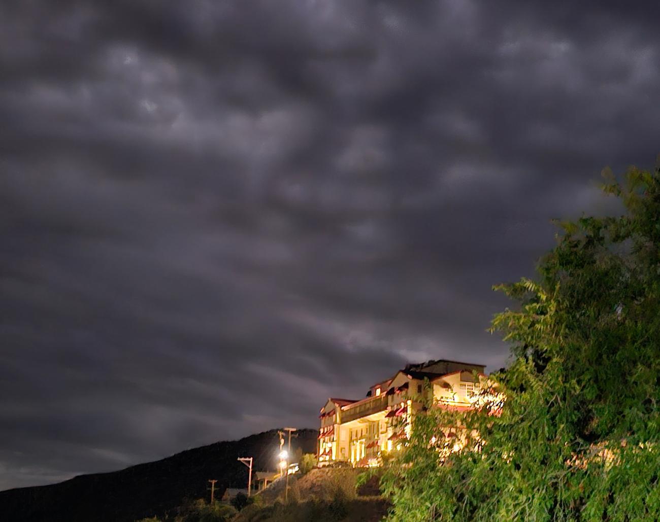 The Jerome Grand Hotel glowing on the hillside at night beneath heavy storm clouds