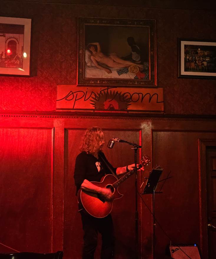 A musician playing guitar under red light at the Spirit Room