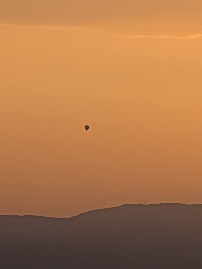 A hot-air balloon tiny in the orange haze